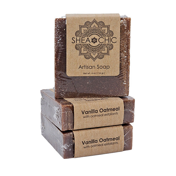 Three bars of Shea Chic Artisan Soap stacked in a pyramid shape, with the top bar labeled 'Vanilla Oatmeal' and the others marked 'Artsan Soap'. All have a brown color and are wrapped in brown paper with a transparent window revealing the soap inside.